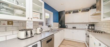 A modern kitchen with white cabinets, a dishwasher, a washing machine, and a coffee maker.