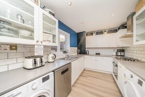 Eine moderne Küche mit weißen Schränken, einem Geschirrspüler, einer Waschmaschine und einer Kaffeemaschine.
