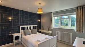 Quarto com cama, mesas de cabeceira, janela com cortinas, radiador e luminária pendente.