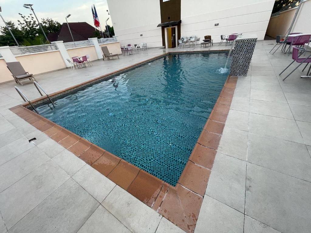 Ein rechteckiger Pool im Freien mit Fliesenrand, umgeben von Liegestühlen und Tischen.