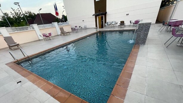 Ein rechteckiger Pool im Freien mit Fliesenrand, umgeben von Liegestühlen und Tischen.