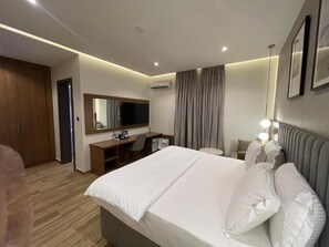 A hotel room with a bed, a desk, a chair, a television, and a wardrobe. - Checkinn Hotel And Resort (Jimeta)