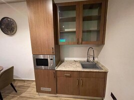 Cozinha compacta com micro-ondas, pia e armários de madeira.