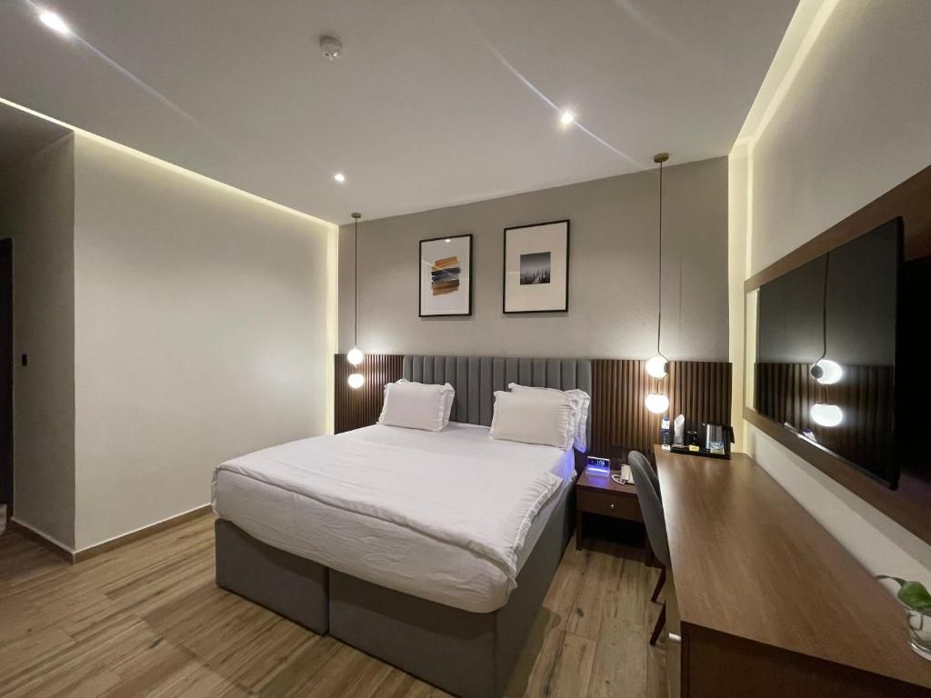 Ein modernes Hotelzimmer mit einem großen Bett, Nachttischen, einem Schreibtisch und einem Flachbildfernseher.
