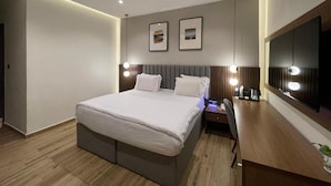 Ein modernes Hotelzimmer mit einem großen Bett, Nachttischen, einem Schreibtisch und einem Flachbildfernseher.