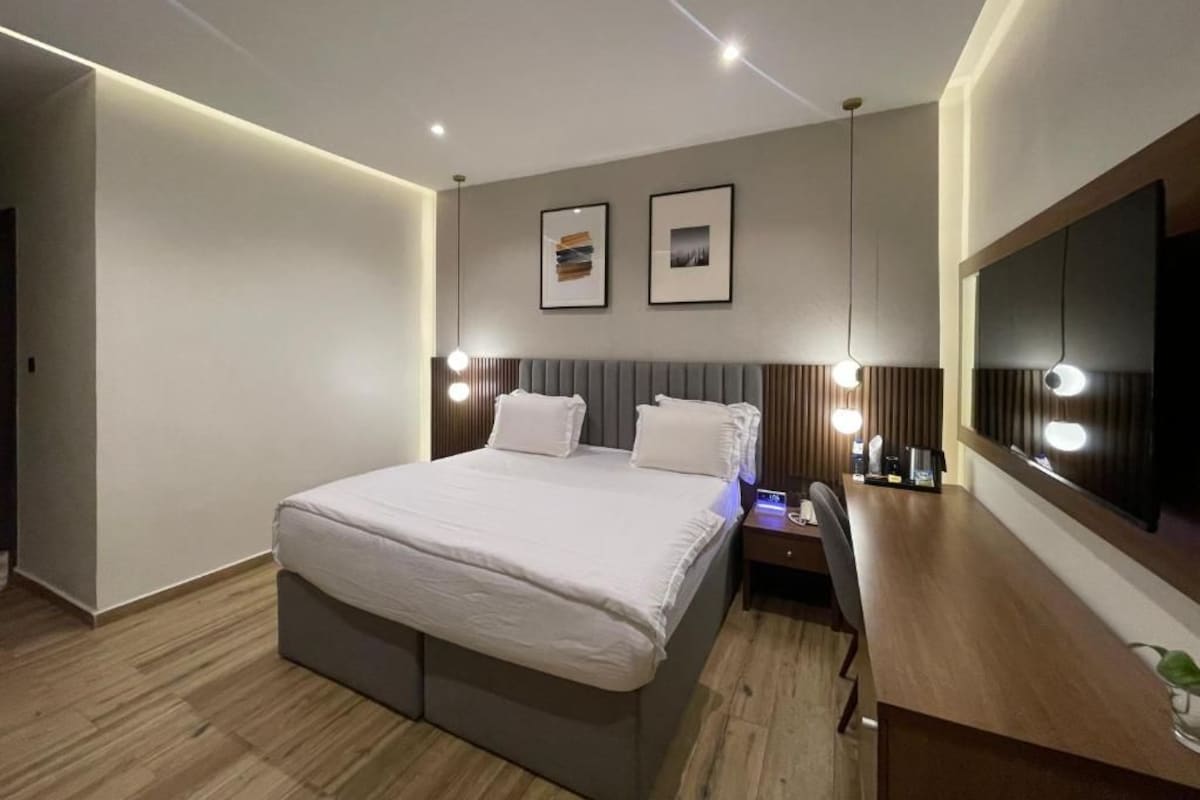 Ein modernes Hotelzimmer mit einem großen Bett, Nachttischen, einem Schreibtisch und einem Flachbildfernseher.