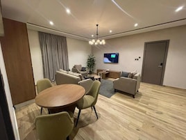 A modern living room with a round wooden table, two sofas, a television mounted on the wall, and a door.