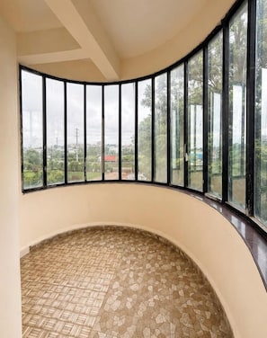 Habitación con pared curva y ventanas amplias, que ofrece vistas a zonas verdes y edificios.