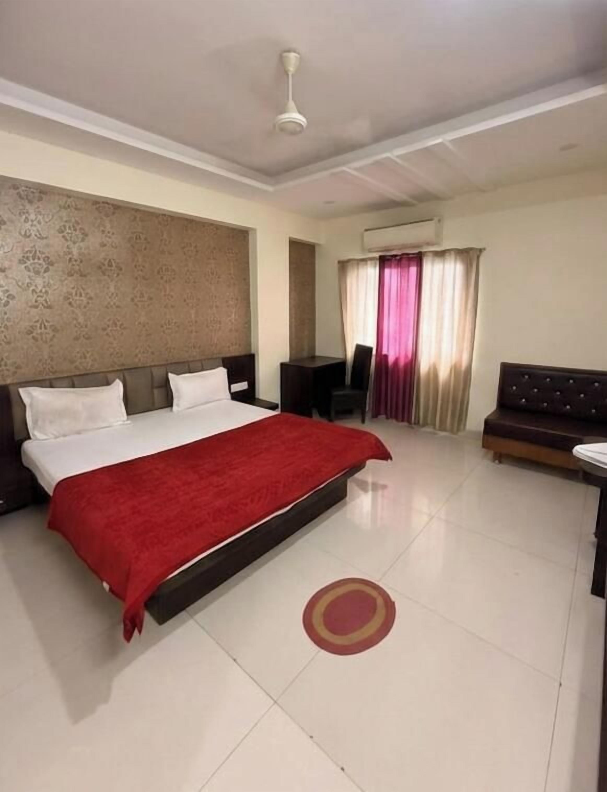 A hotel room with a large bed, a desk, a sofa, and an air conditioning unit.