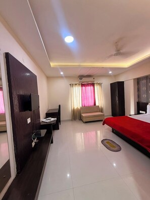 A hotel room with a bed, a desk, a chair, a TV, and a wardrobe. - HR Resort And Hotel (Indore)
