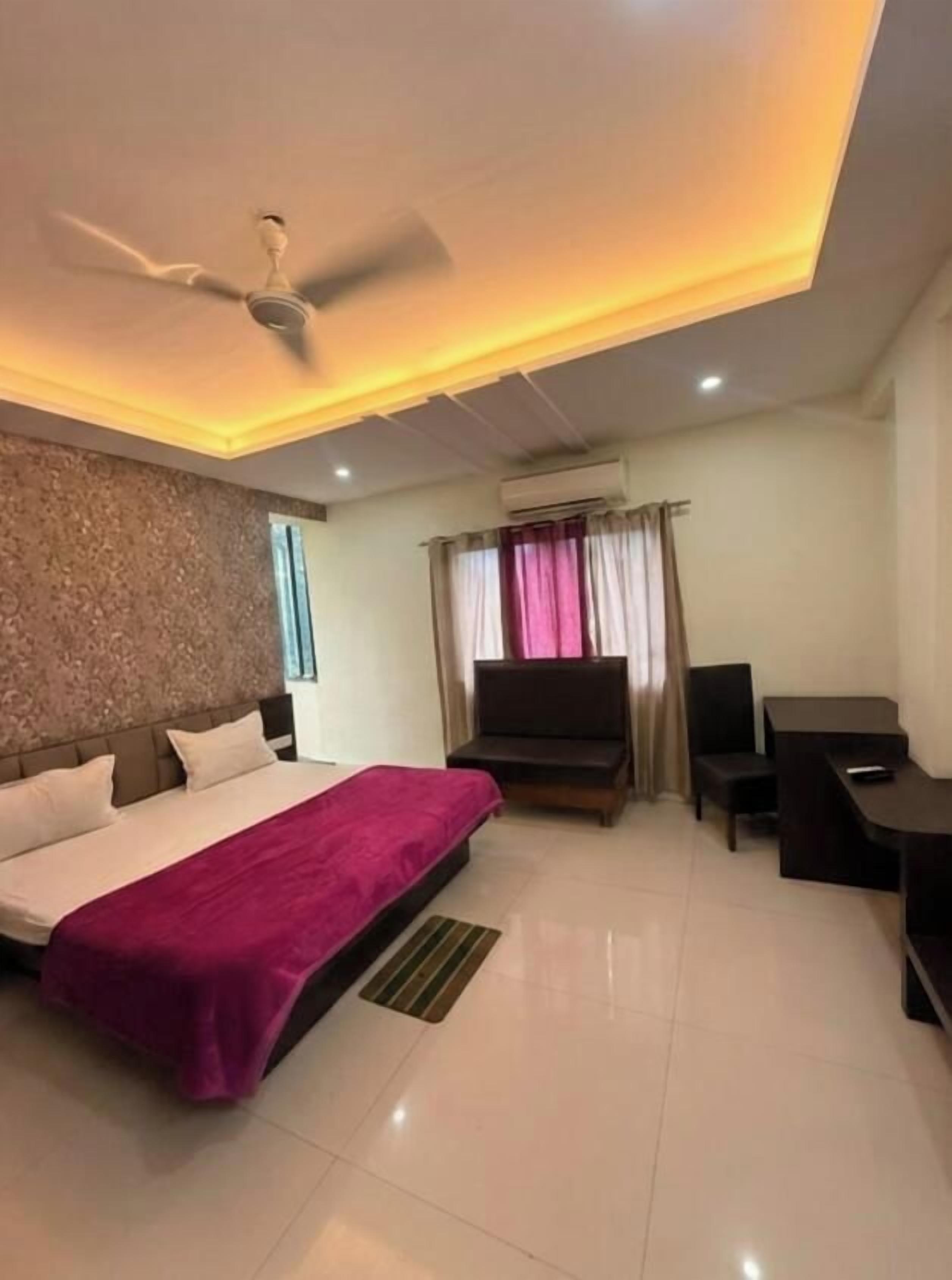 A hotel room with a bed, a desk, a TV, and a ceiling fan.