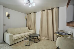 A room with a beige sofa, a small round table with a gold frame, and a chair. - New Apartment Center of Paris/le Marais (Paris)