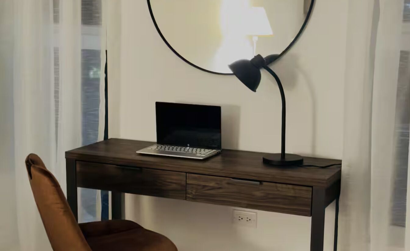 A wooden desk with a laptop and a desk lamp.