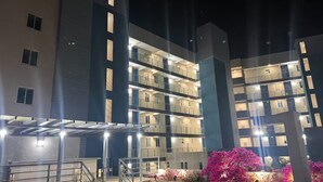 Un immeuble à plusieurs étages doté de balcons, d’un espace extérieur couvert et d’un jardin aménagé avec des fleurs roses.