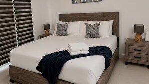 Un lit bien fait, avec une couverture bleu foncé et des oreillers, une tête de lit en bois et des tables de chevet avec des lampes.