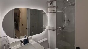 Une salle de bain moderne avec un grand miroir ovale, une douche à parois de verre et des toilettes.
