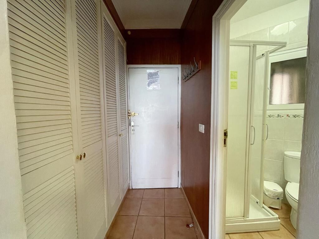 Een smalle gang met een gesloten deur aan het einde, die leidt naar een badkamer met toilet en douche.