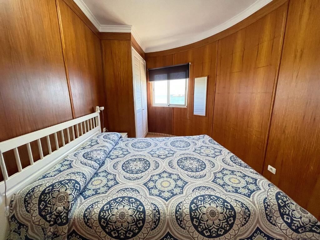 A bedroom with wooden paneling, a bed with patterned bedding, a window with blinds, and a door.