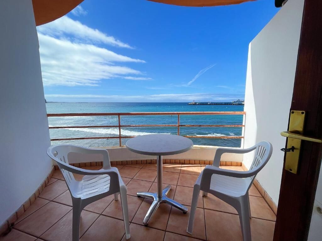 Un balcón con una mesa y dos sillas, con vistas a la costa y un muelle a lo lejos.