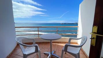 Un balcón con una mesa y dos sillas, con vistas a la costa y un muelle a lo lejos.