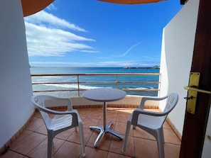 A balcony with a table and two chairs, overlooking a coastal view with a pier in the distance. - Apartment Cristianmar (Arona)