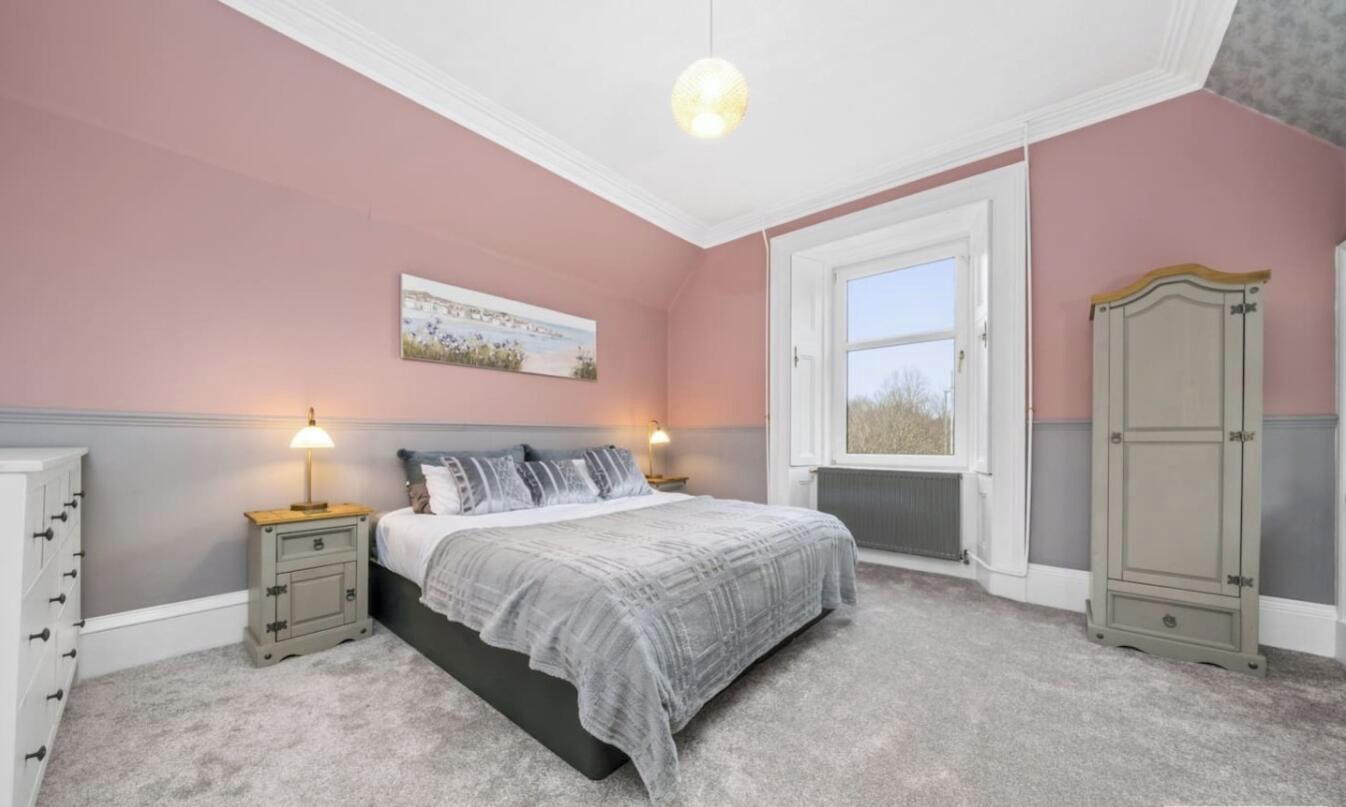 Une chambre à coucher avec un lit, des tables de chevet, une armoire, une fenêtre et un tableau au mur.