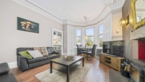 Ein Wohnzimmer mit Sofa, Couchtisch, Fernseher, Kamin und Essbereich.