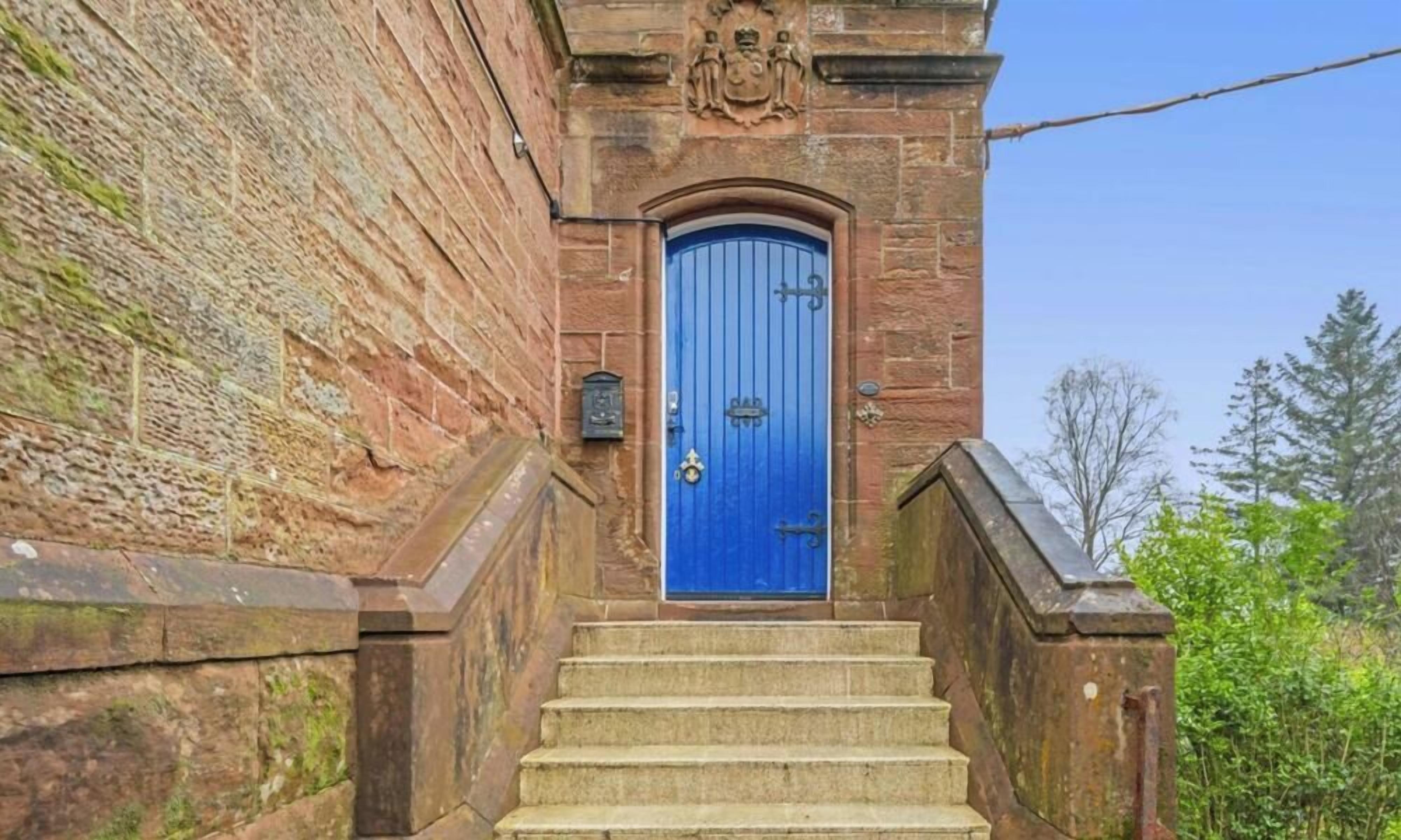 Un bâtiment en pierre avec une porte bleue et un escalier en pierre menant à l’entrée.