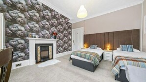 Ein Schlafzimmer mit zwei Betten, einem Kamin und einer Wand mit einem Blumenmuster.