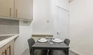 Un pequeño comedor con una mesa dispuesta para dos, una puerta blanca y un salpicadero de azulejos.