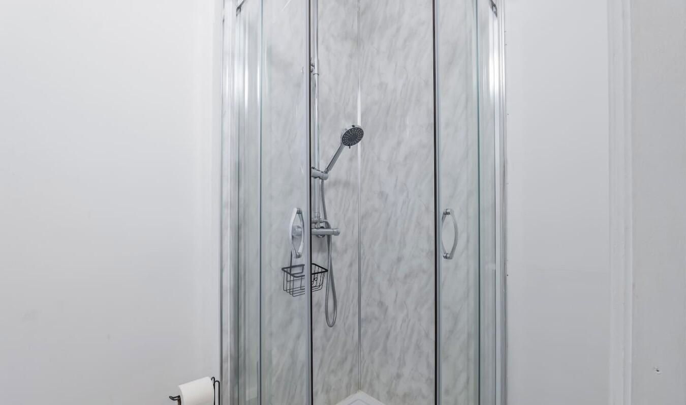 Ducha con mampara de vidrio, cabezal de ducha manual y grifo empotrado.