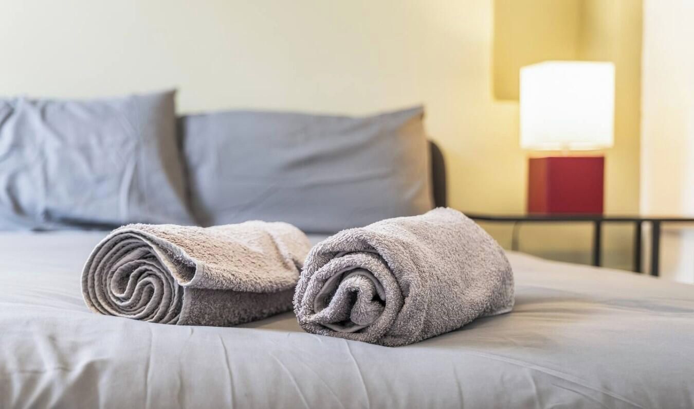 Una cama bien hecha con toallas enrolladas y una lámpara de noche.