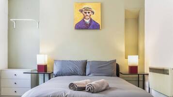 A hotel room with a bed, two bedside tables with lamps, a nightstand, and a painting on the wall.