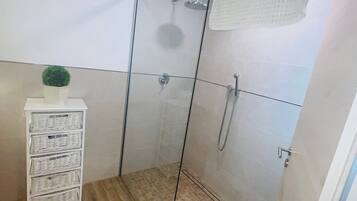 A shower area with a glass door, a white shelf with baskets, and a potted plant.