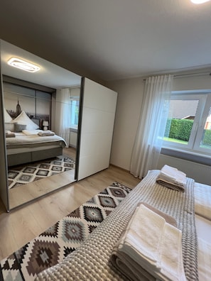 A modern bedroom with a bed, a large mirror, a window with curtains, and a patterned rug. - Apartment 'Waldnest ' with private terrace and Wi-Fi (Walhausen)