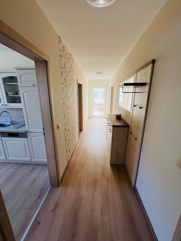 A hallway with a kitchen area on the left, a door with a frosted glass window, and a refrigerator on the right.