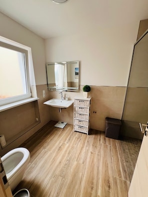 Ein Badezimmer mit Waschbecken, Spiegel, Fenster und einer kleinen Pflanze.