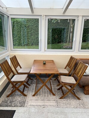 A sunroom with a wooden table and chairs, large windows, and a view of greenery.