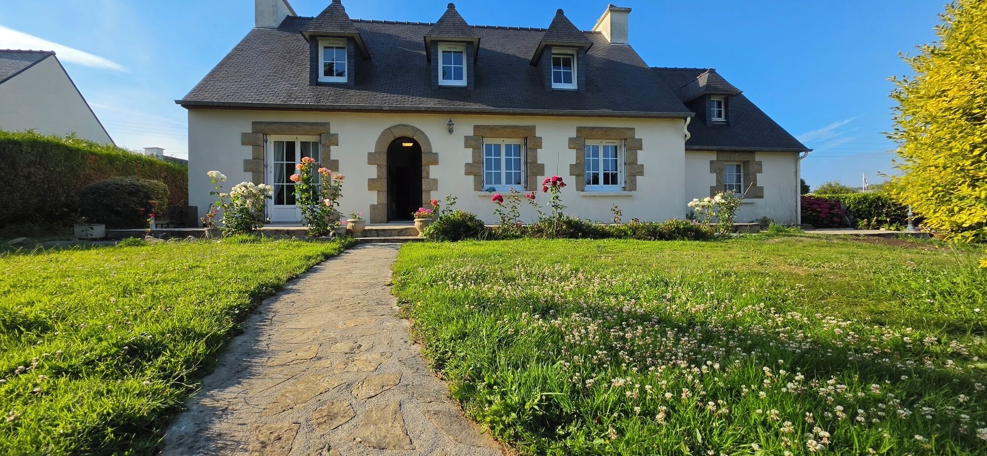 Een huis met twee verdiepingen, met een stenen pad dat naar de ingang leidt, omgeven door een verzorgde tuin met diverse bloemen.