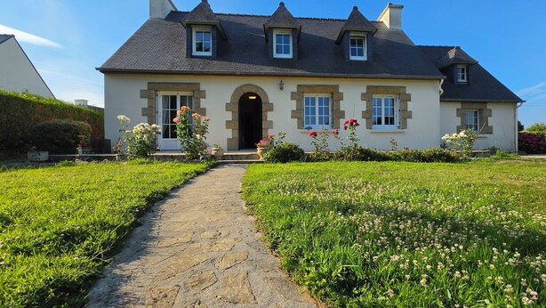 A two-story house with a stone pathway leading to the entrance, surrounded by a well-maintained garden with various flowers. - A family home in Brittany, a ten-minute walk from Paimpol and its harbor (Ploubazlanec)