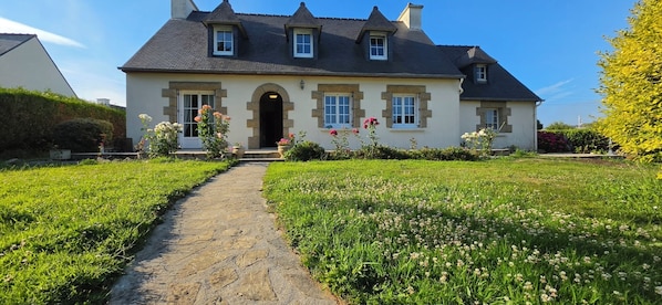 A two-story house with a stone pathway leading to the entrance, surrounded by a well-maintained garden with various flowers. - A family home in Brittany, a ten-minute walk from Paimpol and its harbor (Ploubazlanec)