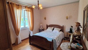 A bedroom with a wooden bed, a nightstand, a lamp, a dresser, and a window with curtains. - A family home in Brittany, a ten-minute walk from Paimpol and its harbor (Ploubazlanec)