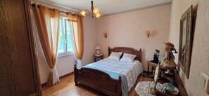 A bedroom with a wooden bed, a nightstand, a lamp, a dresser, and a window with curtains. - A family home in Brittany, a ten-minute walk from Paimpol and its harbor (Ploubazlanec)