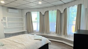Ein Schlafzimmer mit einem Bett, einem schwarzen Nachttisch, einer eingebauten Bank, einem Fenster mit Vorhängen und einer Decke mit Gittermuster.