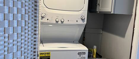 Un espace buanderie compact comprenant un lave-linge et un sèche-linge à chargement frontal, un bac de rangement gris et une cloison en osier.