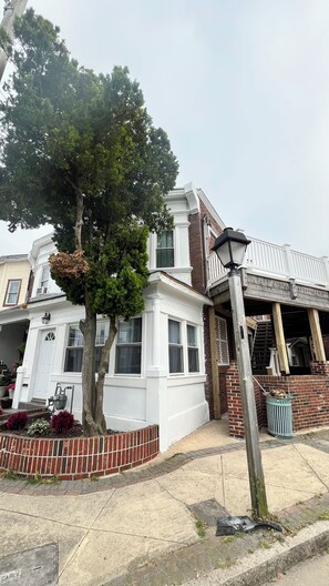 Ein zweistöckiges Gebäude mit weißer Fassade, ein großer Baum davor und eine Holzterrasse.
