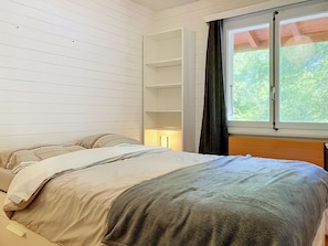 A bedroom with a bed, a nightstand, a window with curtains, and a built-in shelf unit.