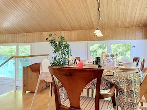 A dining area with wooden furniture, a table set for a meal, and a view of the outdoors through large windows.