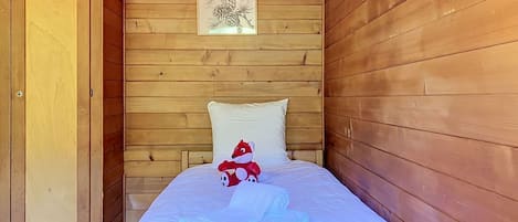 Ein Zimmer in einer Holzhütte mit einem Bett, einer Tür und einem gerahmten Bild an der Wand.