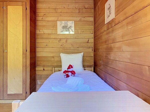 A wooden cabin room with a bed, a door, and a framed picture on the wall.